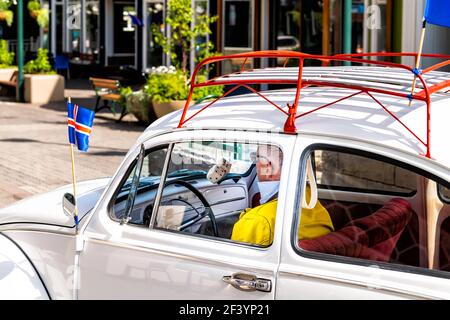 Akureyri, Island - 17. Juni 2018: Stadtstraße mit Mann im Retro-Oldtimer und isländischen Flaggen, die durch Gebäude fahren Stockfoto