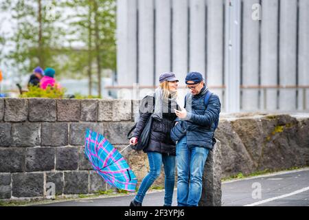 Reykjavik, Island - 19. Juni 2018: Glückliches lächelndes Paar telefoniert am regnerischen Regentag mit Regenschirm von der lutherischen Kirche Hallgrimskirkja in Downt Stockfoto