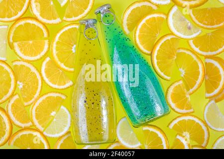Zwei Glasflaschen auf einem hellen tropischen Zitrushintergrund. Blaue und gelbe Getränke mit Samen. Orangenscheiben, Obst-Smoothie. Getränke in Wasser. Sommer Stockfoto