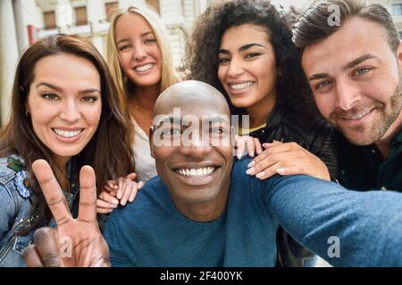 Multiethnische Gruppe von Freunden unter selfie in einer städtischen Straße mit einem schwarzen Mann im Vordergrund. Drei junge Frauen und zwei Männer, legere Kleidung. Stockfoto