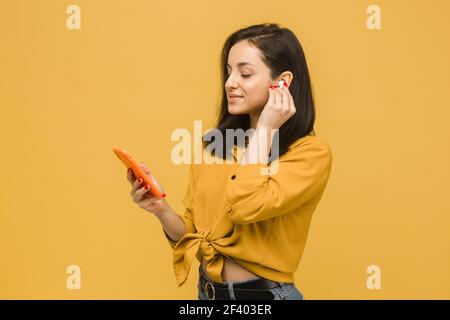 Nahaufnahme Foto von jungen Weibchen ist mit EarPods und Smartphone. Trägt gelbes Hemd, isolierte gelbe Farbe Hintergrund Stockfoto