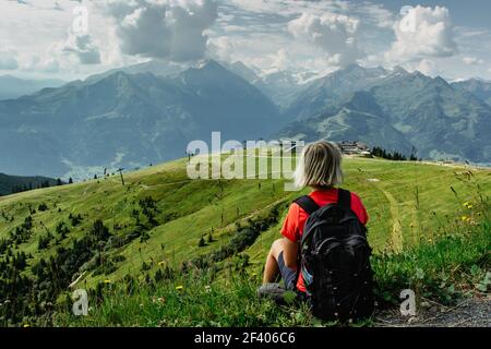 Blonde Mädchen genießen Aussicht während Trekking in Alpen, Austria.Majestic Gipfel der Berge, grüne Wiesen, Blick auf Tal. Aktiv glücklich Rucksacktourist.Reisen Stockfoto