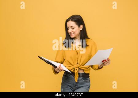 Konzept Foto der Geschäftsfrau hält Papiere. Trägt gelbes Hemd, isolierte gelbe Farbe Hintergrund Stockfoto
