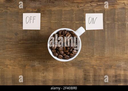 Kaffeebohnen in einer weißen Tasse mit den Worten auf und ab auf Papierstücken auf einem hölzernen Hintergrund. Draufsicht. Kaffee am Morgen Konzept. Stockfoto