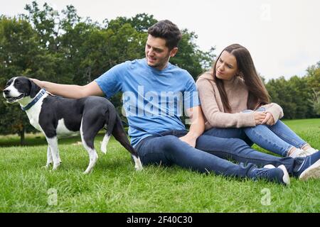 Junges Paar sitzt mit Hund auf Gras in der parken Stockfoto