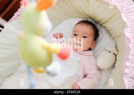 Baby Mädchen zwei Monate alt bei einer Puppe in seiner Krippe suchen Stockfoto