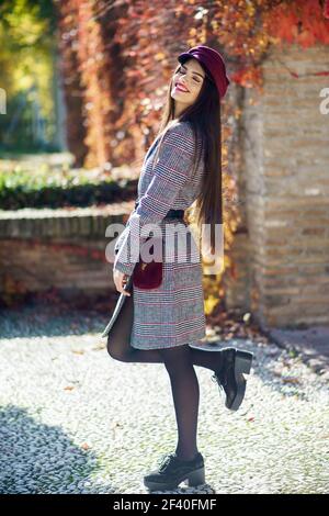 Spanien, Andalusien, Granada. Junge schöne Mädchen mit sehr langen Haaren tragen Wintermantel und Mütze im Herbst Blätter Hintergrund. Lifestyle- und Modekonzept. Stockfoto