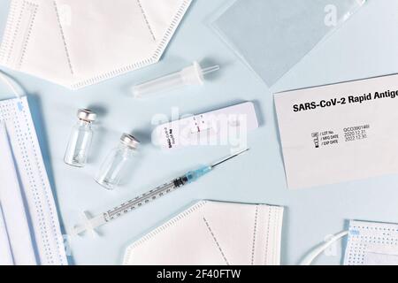 Werkzeuge zur Bekämpfung von Corona Virus Pandemie einschließlich schneller Antigentest, medizinische Gesichtsmasken und Impffläschchen mit Spritze Stockfoto
