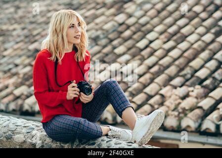 Attraktive junge blonde Frau fotografiert mit einer alten spiegelreflexkamera in einer schönen Stadt. Blonde glückliche Frau sitzt auf städtischen Treppen.. Junge Frau fotografiert mit einer alten Kamera in einer schönen Stadt. Stockfoto