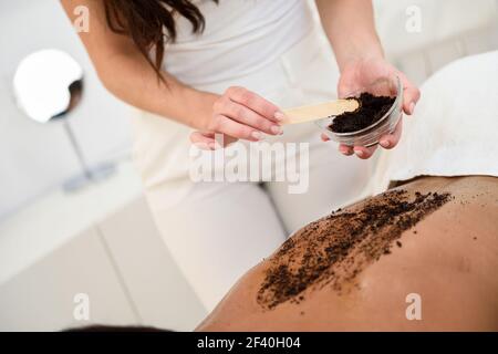 Frau reinigt die Haut des Körpers mit Kaffee Peeling in Spa Wellness Center. Schönheit und ästhetische Konzepte. Stockfoto