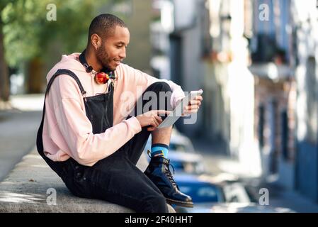 Junger schwarzer Mann mit digitalen Tablet im städtischen Hintergrund. Lifestyle- und Technologiekonzepte. Junger schwarzer Mann mit digitalen Tablet im städtischen Hintergrund. Stockfoto