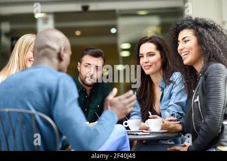 Multirassische Gruppe von fünf Freunden mit einem Kaffee zusammen. Drei Frauen und zwei Männer im Café, reden, lachen und genießen ihre Zeit. Lifestyle- und Freundschaftskonzepte mit echten Menschen-Modellen. Multirassische Gruppe von fünf Freunden mit einem Kaffee zusammen Stockfoto