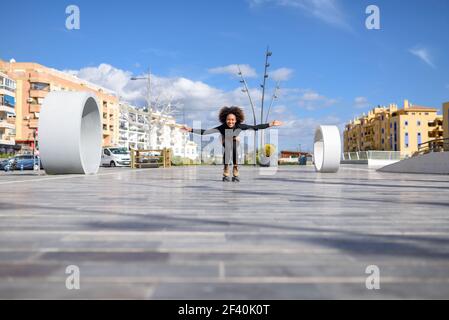 Junge fit schwarze Frau auf Rollschuhe Reiten im Freien auf städtischen Straße. Lächelndes Mädchen mit afro Frisur Rollerblading an sonnigen Tag. Schwarze Frau auf Rollschuhe Reiten im Freien auf städtischen Straße Stockfoto