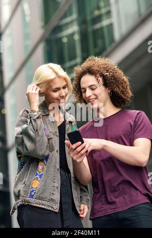 Glückliches Paar mit Smartphone im städtischen Hintergrund. Junger Mann und Frau tragen legere Kleidung in einer Londoner Straße. Glückliches Paar mit Smartphone im städtischen Hintergrund. Stockfoto