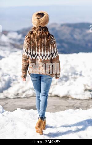 Rückansicht einer Frau, die im Winter die verschneiten Berge genießt, in der Sierra Nevada, Granada, Spanien. Frau trägt Winterkleidung. Junge Frau genießt die verschneiten Berge im Winter Stockfoto