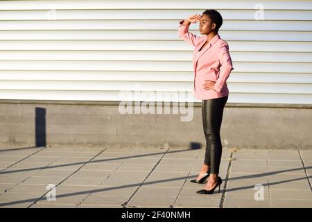 Schwarze Frau, Modell der Mode, auf der Stadtmauer stehend. afroamerikanische Frauenanzug mit rosa Jacke mit Sonnenuntergang Licht.. Schwarze Frau, Modell der Mode, auf der Stadtmauer stehend Stockfoto
