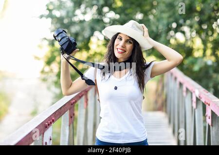 Schöne Wanderer junge Frau fotografiert mit einer spiegellosen Kamera, trägt Strohhut, Wandern auf dem Land.. Wanderfrau, die mit einer spiegellosen Kamera fotografiert Stockfoto