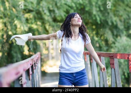 Schöne Wanderer junge Frau mit Rucksack, mit blauen Augen, trägt Strohhut, Wandern auf dem Land und Spaß auf einer ländlichen Brücke.. Frau mit Rucksack auf ländliche Brücke stehen. Stockfoto