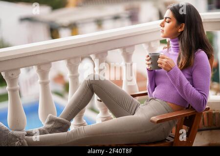 Perserin sitzt in einem Sessel auf ihrem Balkon mit einer Tasse Kaffee. Perserin auf ihrem Balkon mit einer Tasse Kaffee Stockfoto