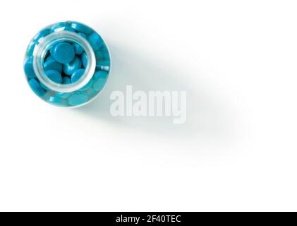 Glas- oder Plastikflasche mit engem Hals, gefüllt mit blauen Pillen und Tabletten, isoliert auf einem großen weißen Hintergrund mit Tropfenschatten. Blick von oben Stockfoto