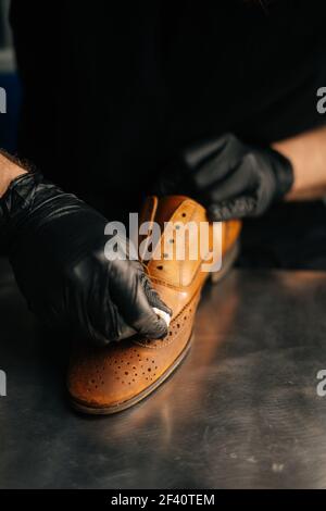 Nahaufnahme Hände des Schuhmachers tragen schwarze Latexhandschuhe reiben alte hellbraune Lederschuhe für spätere Restaurierung. Stockfoto