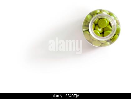 Glas- oder Plastikflasche mit schmalem Hals, gefüllt mit grünen Tabletten und Tabletten isoliert auf einem großen weißen Hintergrund mit Schlagschatten. Blick von oben Stockfoto