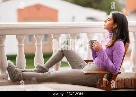 Perserin sitzt in einem Sessel auf ihrem Balkon mit einer Tasse Kaffee. Perserin auf ihrem Balkon mit einer Tasse Kaffee Stockfoto