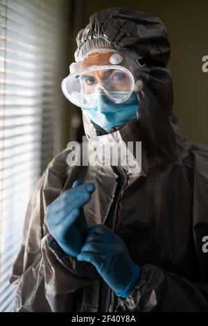 Besorgter Arzt oder Laborant in PSA Persönliche Schutzausrüstung in der Nähe eines Krankenhausfensters. Ärztin in persönlicher PSA-Schutzausrüstung Stockfoto
