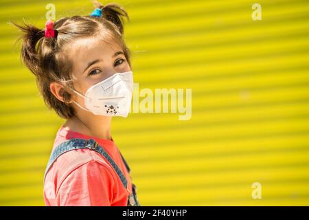 Happy Child Mädchen trägt eine Schutzmaske gegen Coronavirus während Covid-19 Pandemie. KN95 Maske.. Kindermädchen trägt eine Schutzmaske gegen Coronavirus während Covid-19 Pandemie Stockfoto