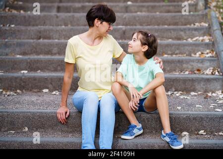 Mutter und Tochter mittleren Alters sitzen auf der Straße auf städtischen Treppen. Mutter und Tochter mittleren Alters sitzen auf der Straße Stockfoto