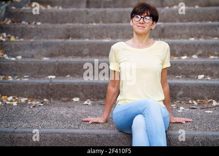 Frau mittleren Alters sitzen auf der Straße auf städtischen Treppen. Schöne Frau mittleren Alters sitzen auf der Straße Stockfoto