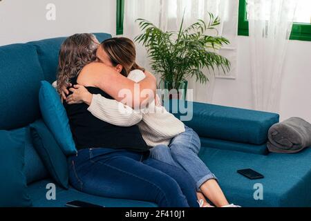 Ältere Mutter und junge Tochter kuscheln liebevoll auf dem Sofa Zu Hause Stockfoto