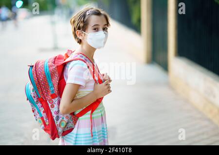 Neun Jahre altes Mädchen geht zurück in die Schule trägt eine Maske und eine Schultasche im Freien.. Neun Jahre altes Mädchen geht zurück in die Schule mit einer Maske und einer Schultasche. Stockfoto