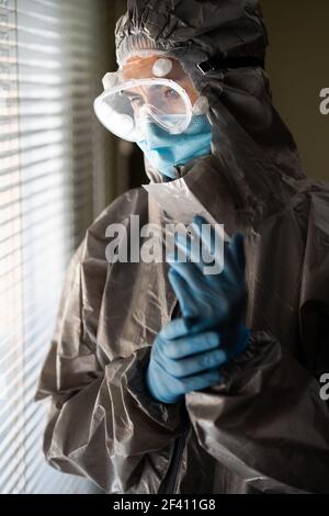Besorgter Arzt oder Laborant in PSA Persönliche Schutzausrüstung in der Nähe eines Krankenhausfensters. Ärztin in persönlicher PSA-Schutzausrüstung Stockfoto
