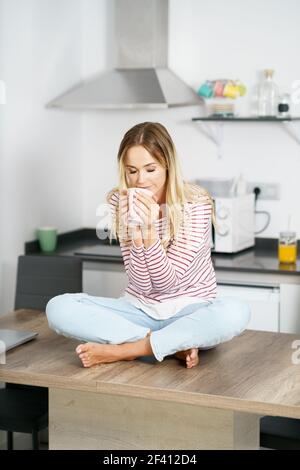 Junge kaukasische Frau riecht eine Tasse Kaffee zu Hause.. Junge Frau hält eine Tasse Kaffee zu Hause. Stockfoto