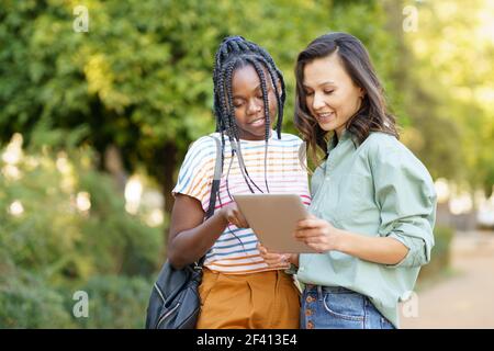 Zwei multiethnische Frauen Beratung etwas auf einem digitalen Tablet im Freien.. Zwei multiethnische Frauen beraten sich auf einem digitalen Tablet. Stockfoto