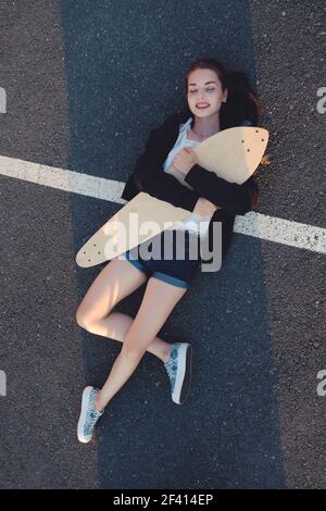 Skateg Mädchen liegend mit ihrem Longboard auf Asphalt Straßenoberfläche über Ansicht. Skateg Mädchen liegend mit ihrem Longboard auf Asphalt Straßenoberfläche Stockfoto