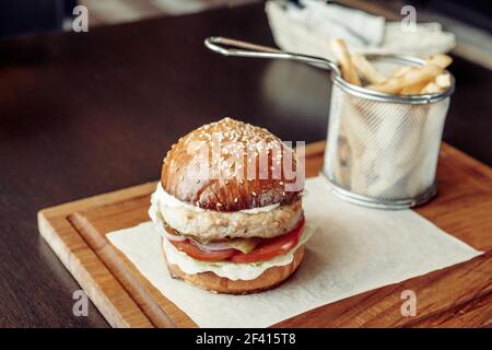 Hähnchenburger mit Tomate auf einem Stück Papier auf einem rustikalen Holzteller im Straßencafé serviert. Burger mit Tomate auf einem Stück Papier auf einem rustikalen Holzteller serviert Stockfoto