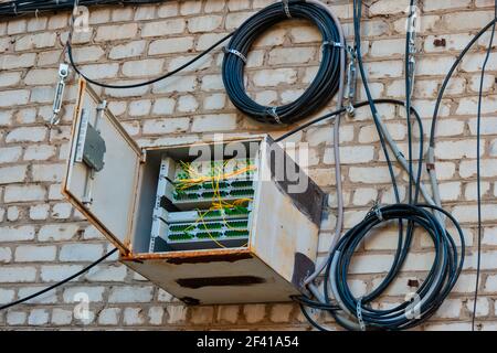 Witterungsversiegelte Box mit Glasfaser-Schalter an der Wand des Wohngebäudes und Spulen von geschützten Drähten in der Nähe hängen platziert. Witterungsversiegelte Box mit Glasfaser-Schalter an der Wand des Wohngebäudes platziert Stockfoto