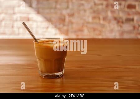 Flacher weißer Kaffee aus transparentem Glas auf Holztisch. Es ist Espresso-basierte Kaffee-Getränk, bestehend aus Espresso mit Mikroschaum gedämpfter Milch mit kleinen Blasen mit einer glänzenden oder samtigen Konsistenz.. Flacher weißer Kaffee aus transparentem Glas auf dem Tisch im Café. Es ist ein Espresso-basiertes Kaffeegetränk, bestehend aus Espresso mit gedämpfter Mikroschaum-Milch mit feinen Blasen mit einer glänzenden oder samtigen Konsistenz Stockfoto