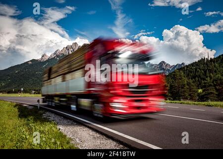 Holz Lkw Rast auf der Autobahn im Hintergrund die Alpen. Lkw Auto in Bewegungsunschärfe. Stockfoto