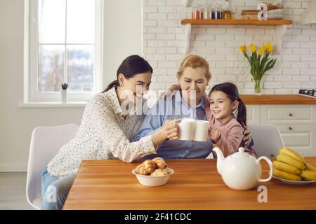 Glückliche ältere Frau trinkt Tee mit Tochter und Enkelin zu Hause in der Küche sitzen. Stockfoto