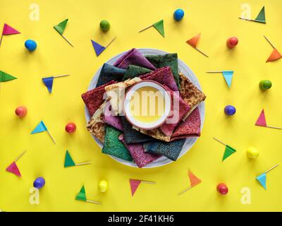 Rainbow Party, Tischaufbau. Lebendige Crepes auf Teller mit Honig. Partytisch, gelbe Papiertischdecke mit farbigen Fahnen. Regenbogen als Symbol für Stockfoto