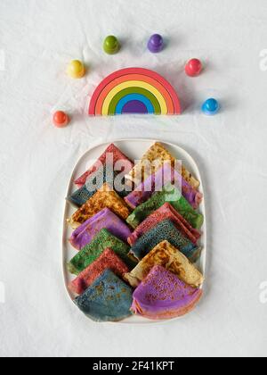 Rainbow Party, Tischaufbau. Lebhafte Crepes auf dem Platz. Aus weißer textiler Baumwolle Tischdecke. Holzfiguren und Holzschnitzelbogen als Symbol des Mitgefühls Stockfoto