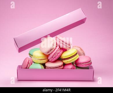 Bunte süße Makronen oder Makronen, aromatisierte Kekse sind in der Pappschachtel auf dem rosa Hintergrund. Stockfoto
