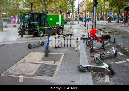 Vermietung Elektroroller geparkt oder auf anarchische Weise auf dem Bürgersteig der Champs-Elysées, Paris, Frankreich gedumpt. Reinigung Auto auf der Rückseite Stockfoto