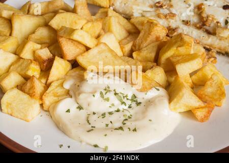 Nahaufnahme von Aioli-Sauce mit Petersilie, begleitet von Kartoffeln und Fisch auf einem Teller. Hausgemachtes Essen. Stockfoto