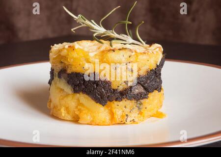 Nahaufnahme eines frischen Rosmarinzweiges auf einem Butterkartoffelkuchen mit schwarzem Pudding, Schokolade und Käsecreme auf einem Teller. Hausgemachte Rezepte. Stockfoto