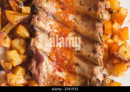 Nahaufnahme eines leckeren gekochten Gerichts mit gebackenen Schweinefleischrippen in einer Knoblauchsauce, Öl, Essig und heißen Gewürzen mit Kartoffeln. Essen und Fleisch. Stockfoto