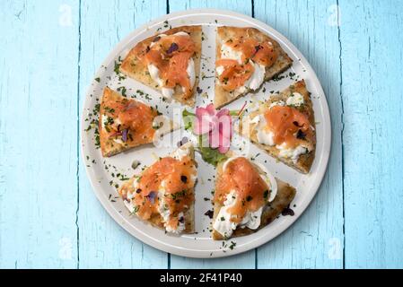 Pizza mit Lachs und Mozzarella burrata Käse, sechs Scheiben in weißem Teller auf hellblauem Holzbrett Hintergrund, flach in Draufsicht Stockfoto